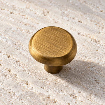 Soft pebble cabinet knob in antique brushed brass on limestone