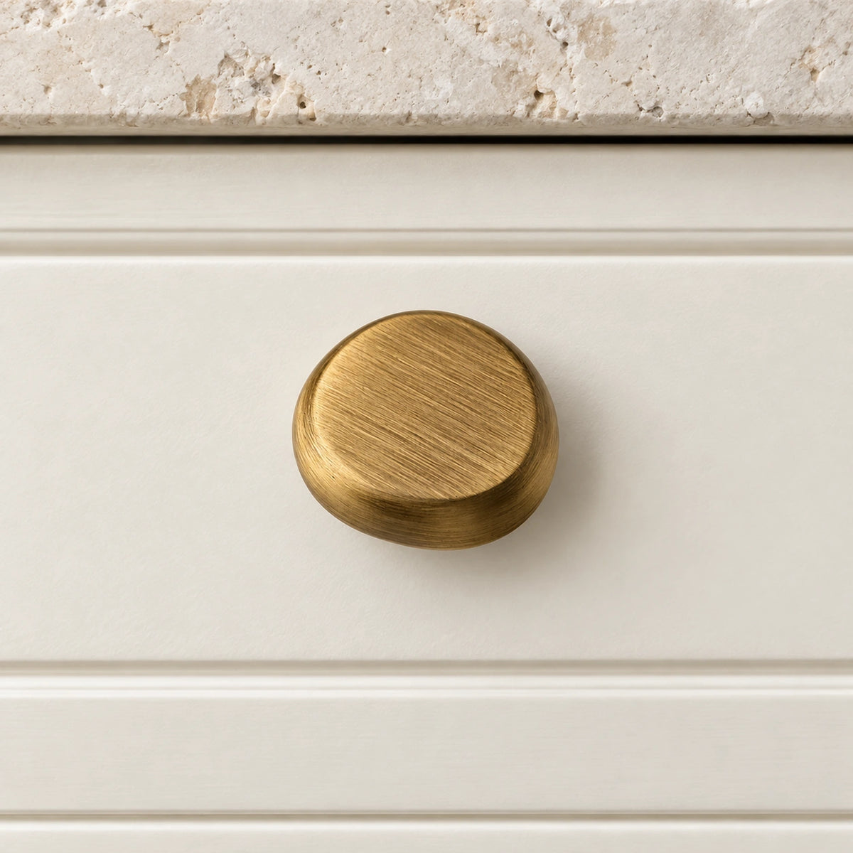Antique brass pebble cabinet knob mounted on an ivory drawer
