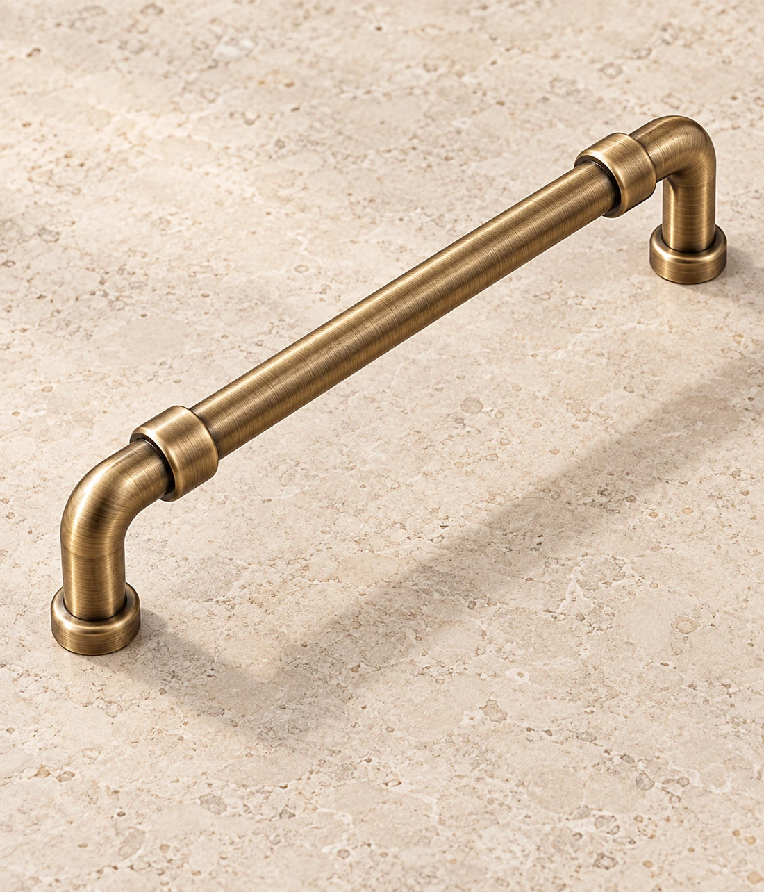 Antique brass pipe cabinet pull with coupling collars on warm limestone