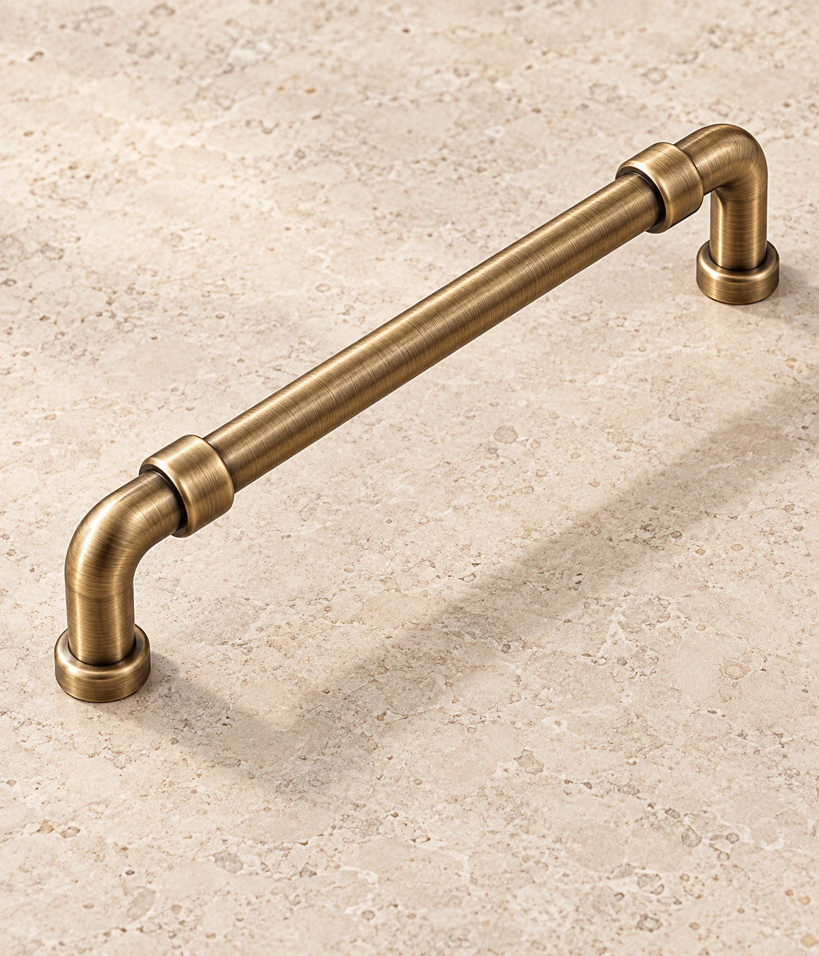 Antique brass pipe cabinet pull with coupling collars on warm limestone