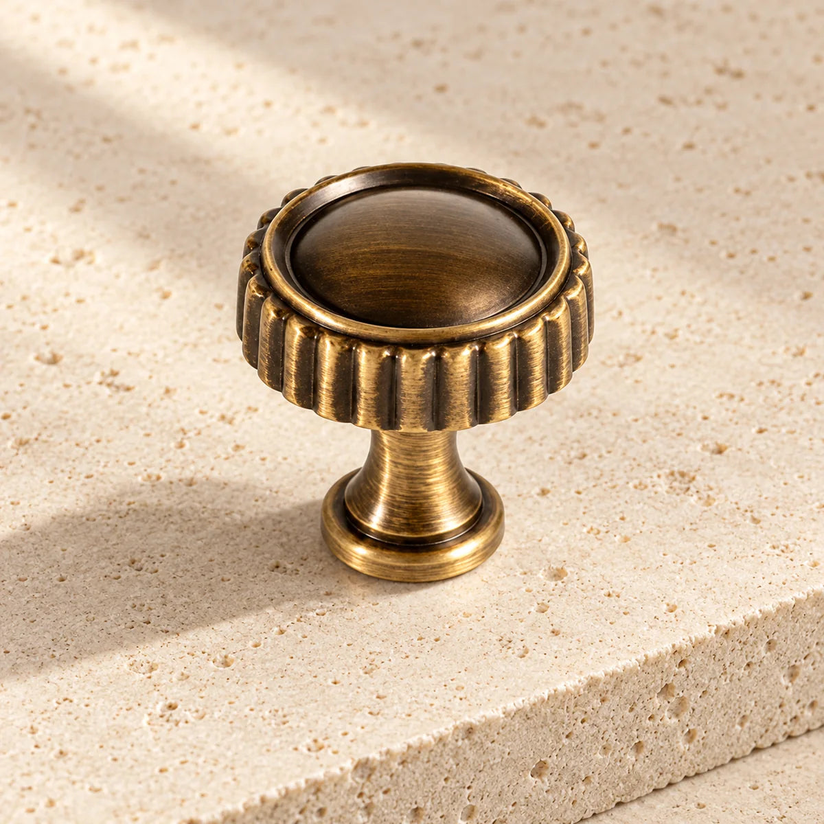 Antique brass ridged cabinet knob with a rounded inset face on pale limestone.