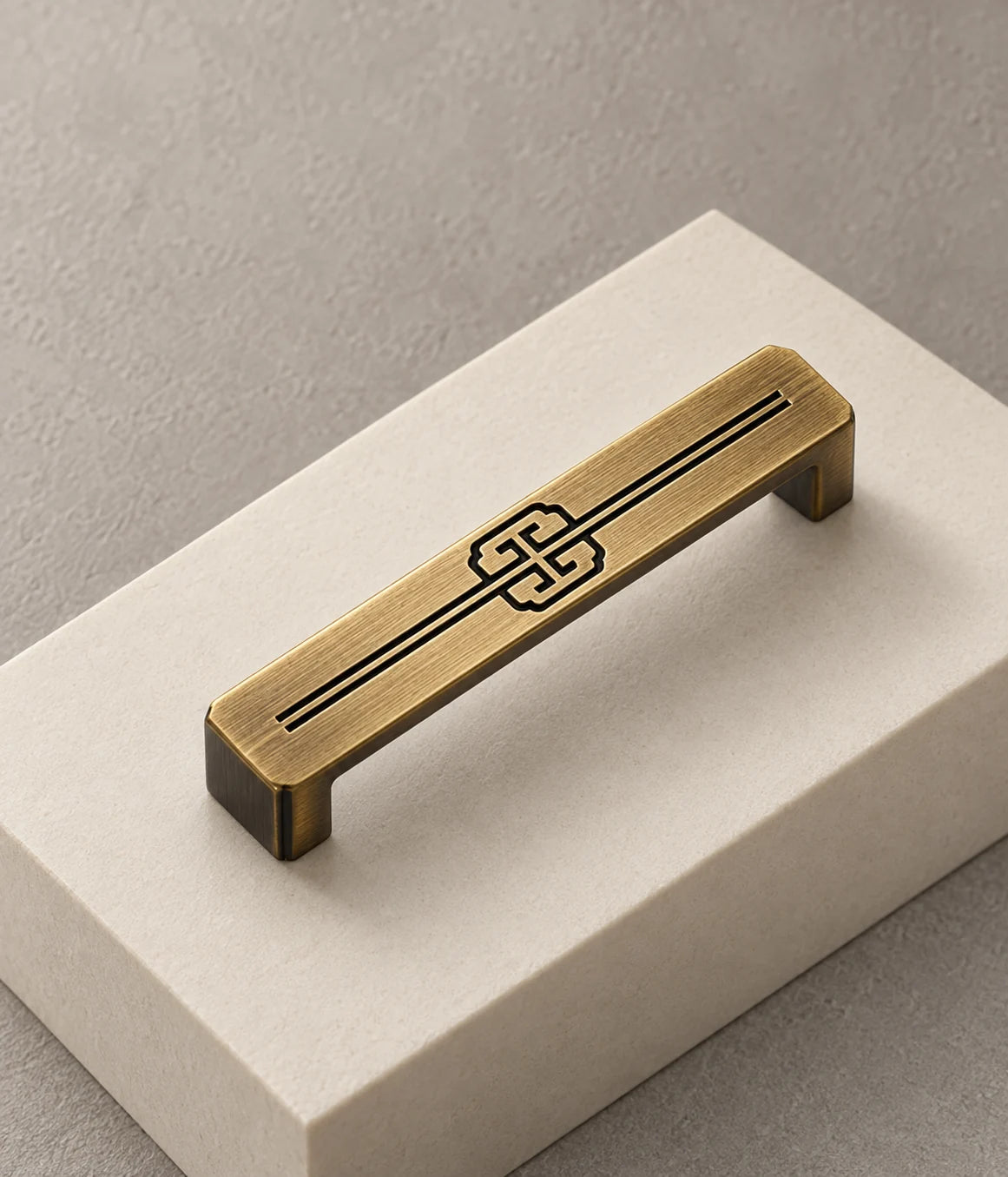 Recessed scroll motif and fine linear detailing on a rectangular antique brass pull