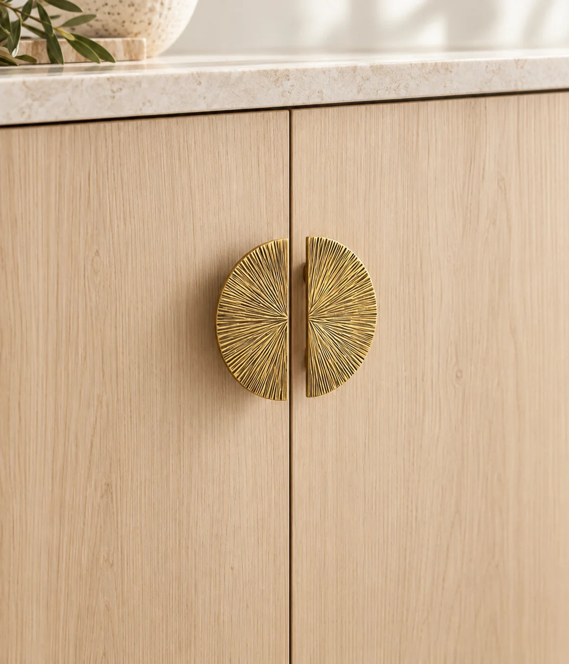 Two antique brass radial half-moon pulls facing each other on pale oak cabinet doors