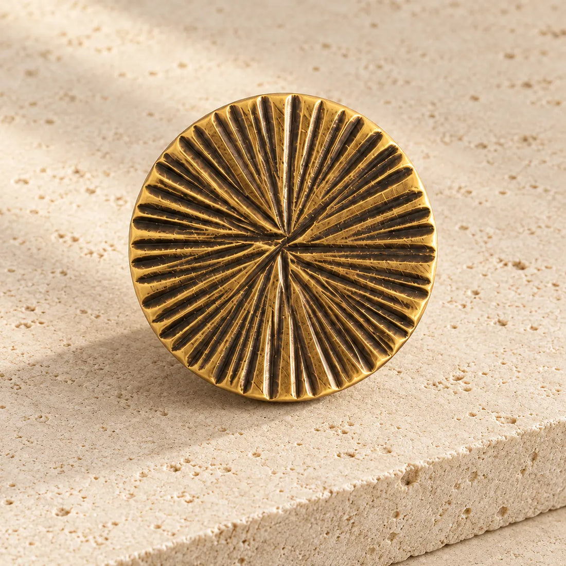 antique brass radial round cabinet knob on pale limestone.