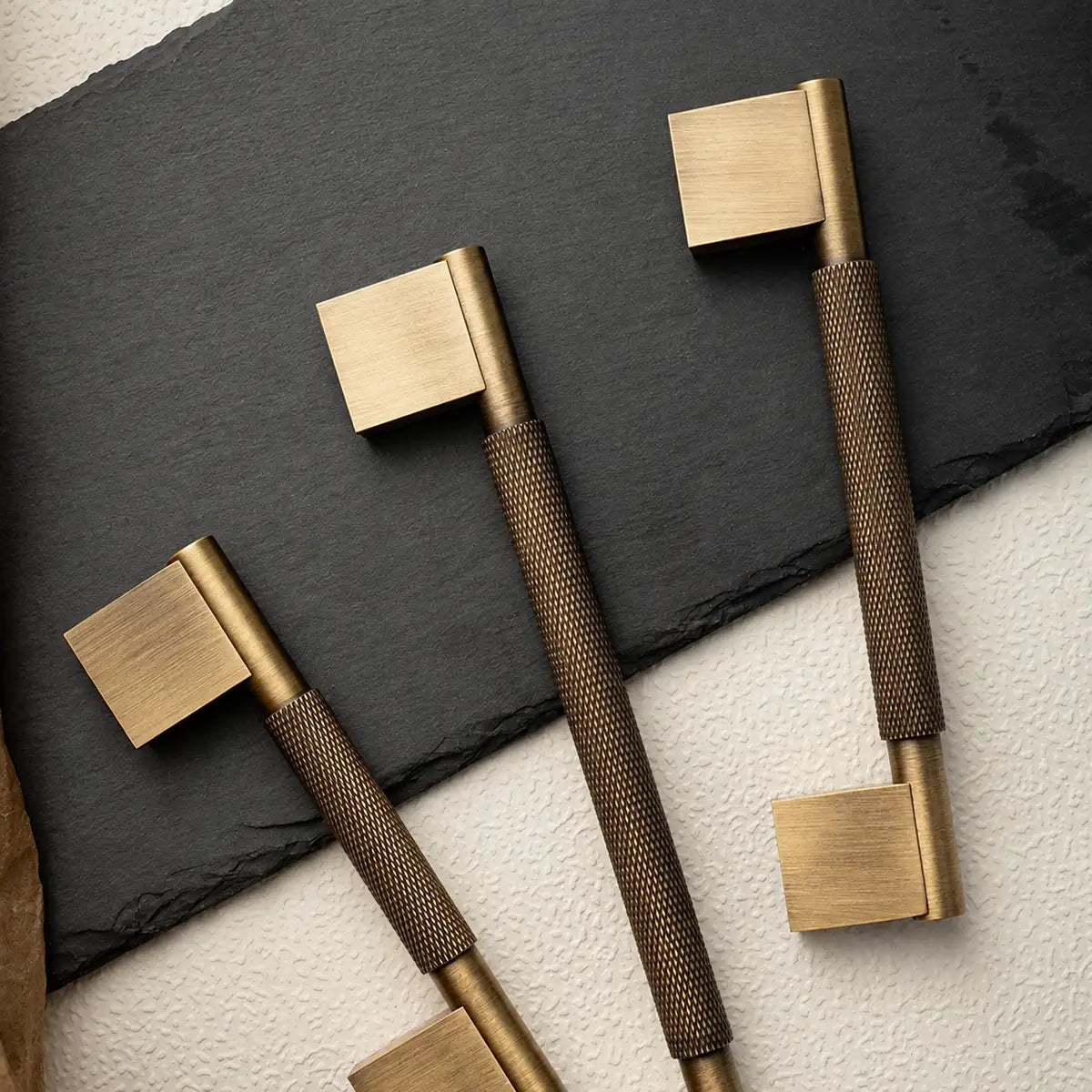 Antique brass knurled cabinet handles with rectangular mounting blocks on slate and cream texture