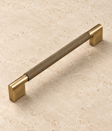 Antique Brass Rectangular-Base Knurled Cabinet Pulls on warm ivory limestone