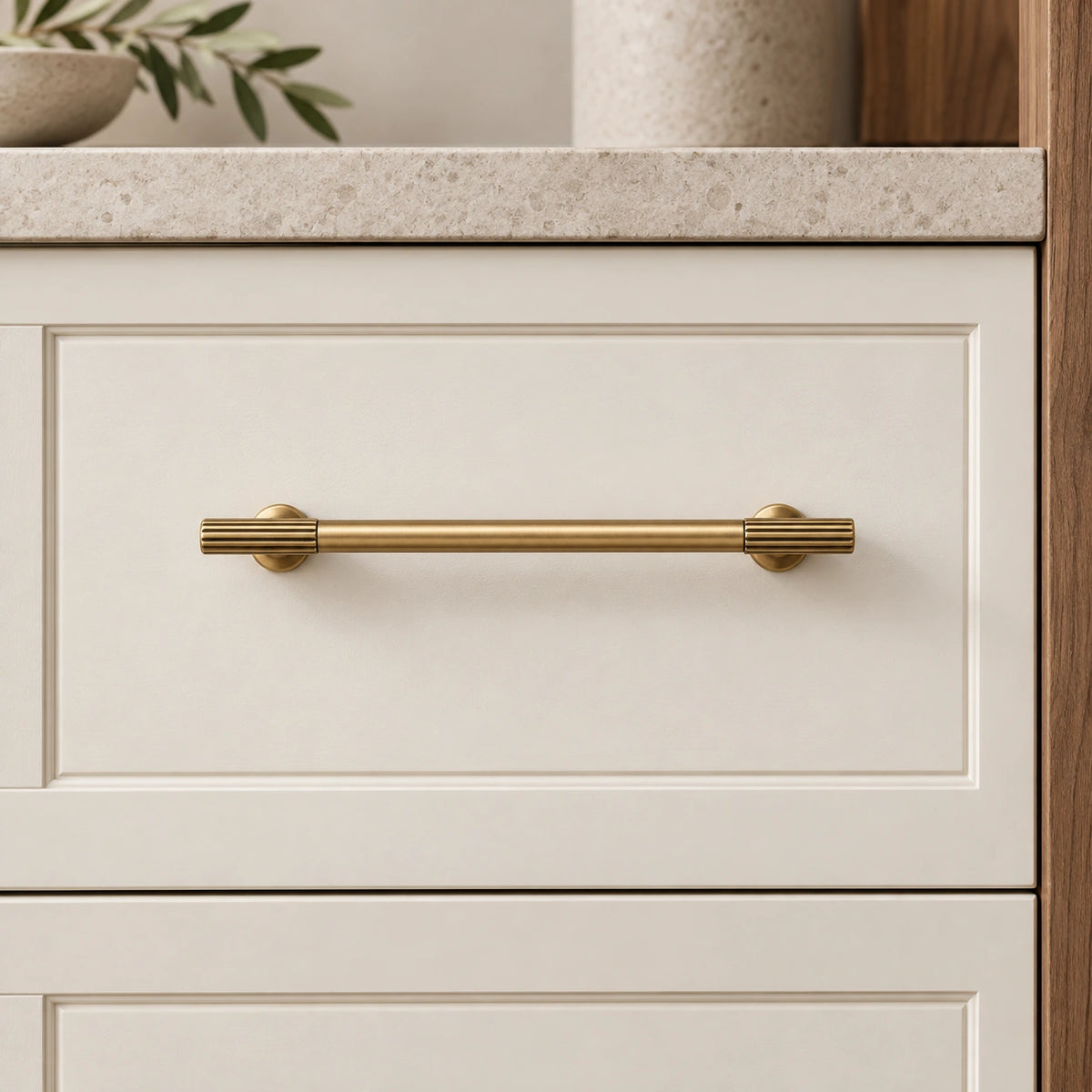 Reeded-end antique brass cabinet pull mounted horizontally on a cream drawer
