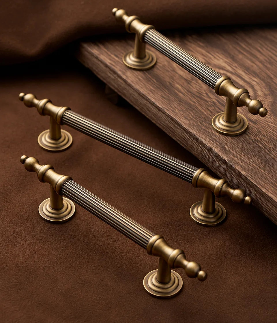 Three antique brass reeded finial cabinet pulls on a wooden surface