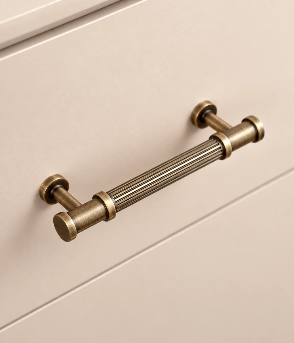 Antique brass reeded pull mounted on a cream cabinet drawer