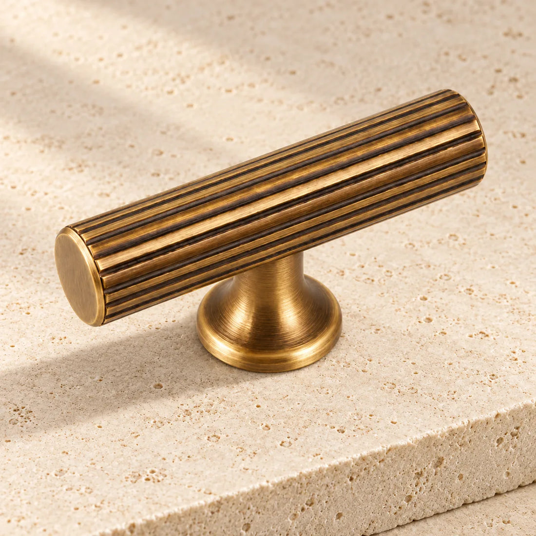 antique brass reeded t bar cabinet knob on pale limestone.
