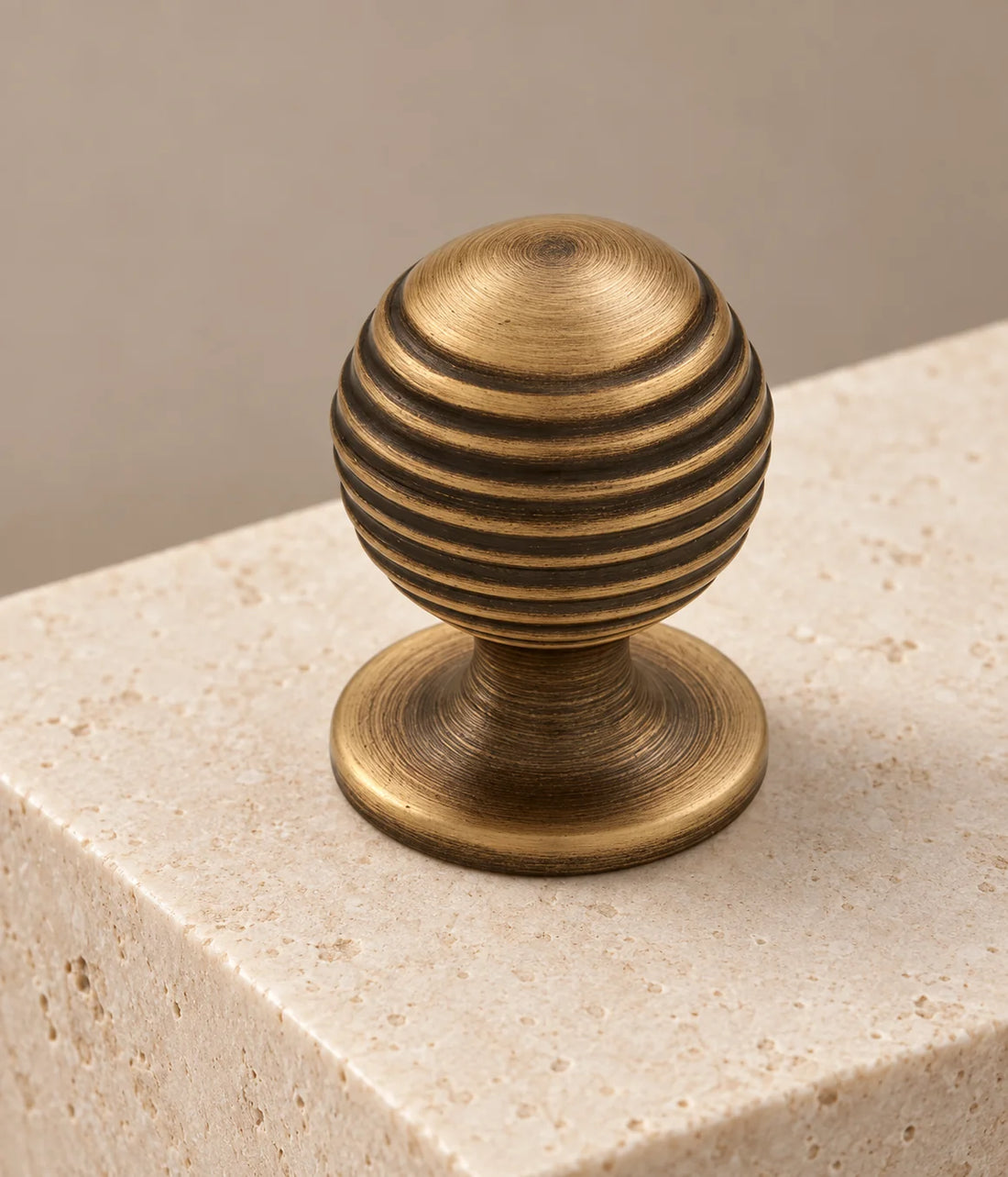 Two sizes of antique brass ribbed ball cabinet knobs on limestone