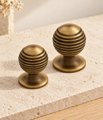Two sizes of antique brass ribbed ball cabinet knobs on limestone