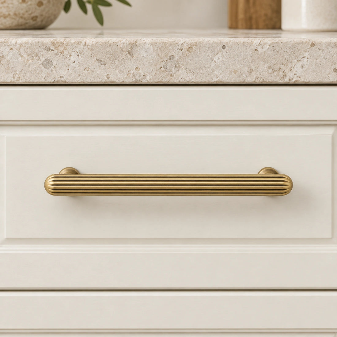 Antique brass ribbed cabinet pulls and fluted knob arranged on limestone