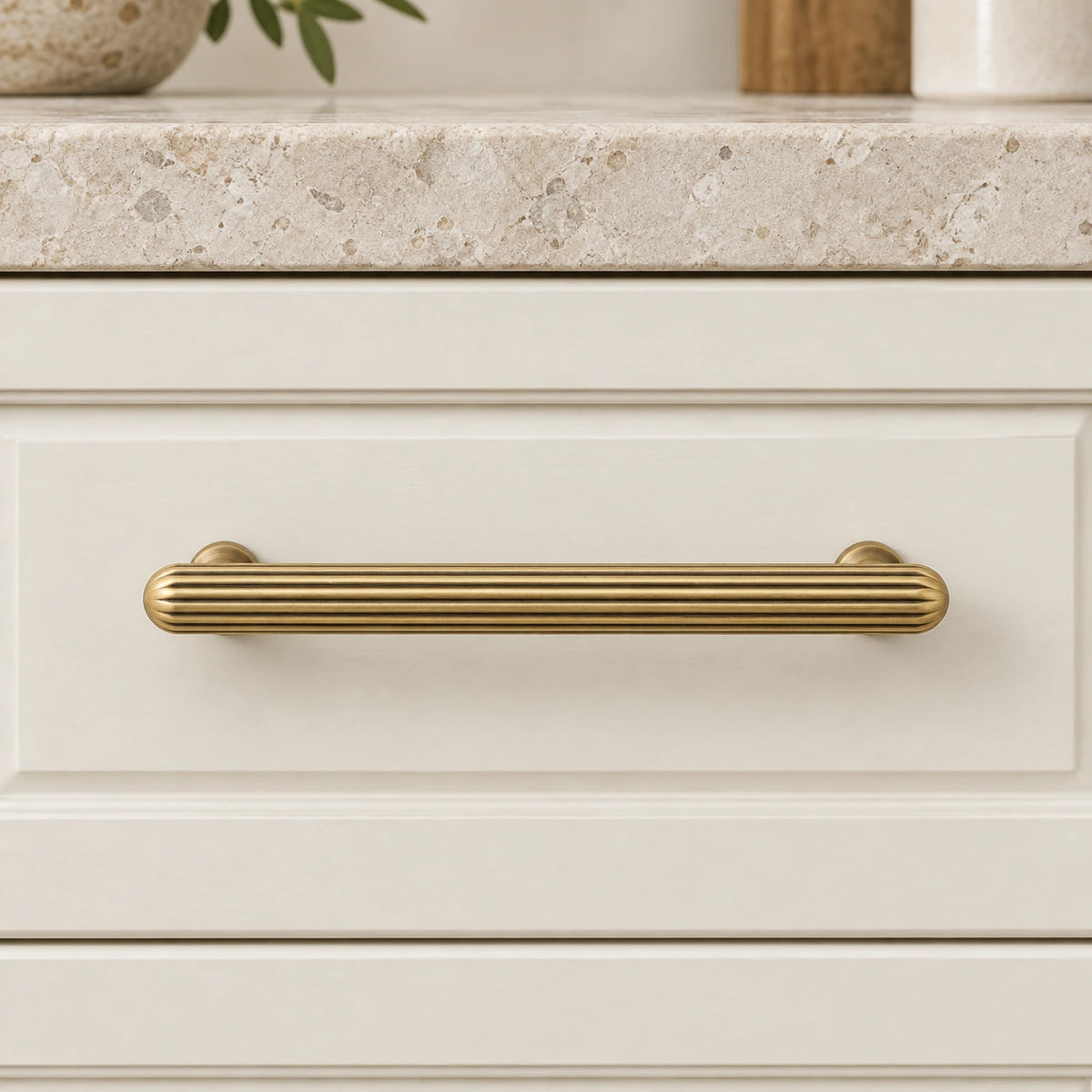 Antique brass ribbed pull and fluted knob mounted on cream cabinet drawers
