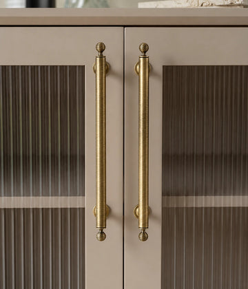 Antique brass cabinet pulls with ribbed ball finials installed on cream ribbed-glass cabinet doors