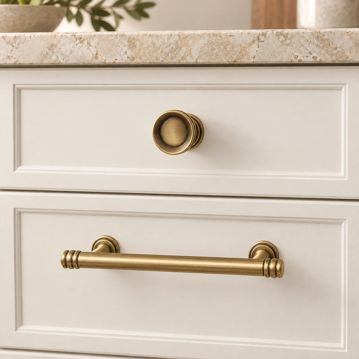 Antique brass ring-cap pull and recessed knob mounted on ivory cabinet drawers