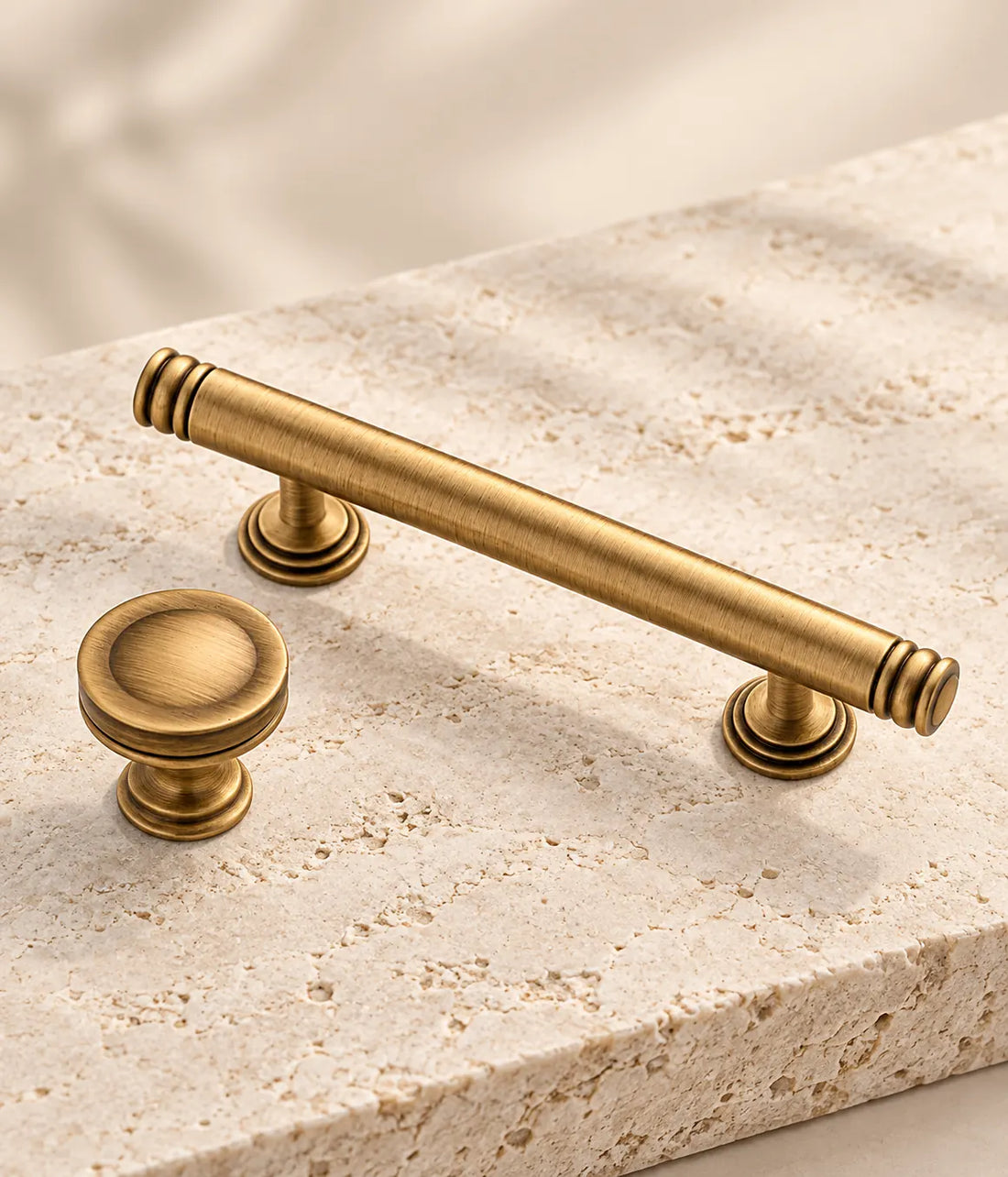 Antique brass ring-end cabinet pulls and dished knobs arranged on limestone blocks