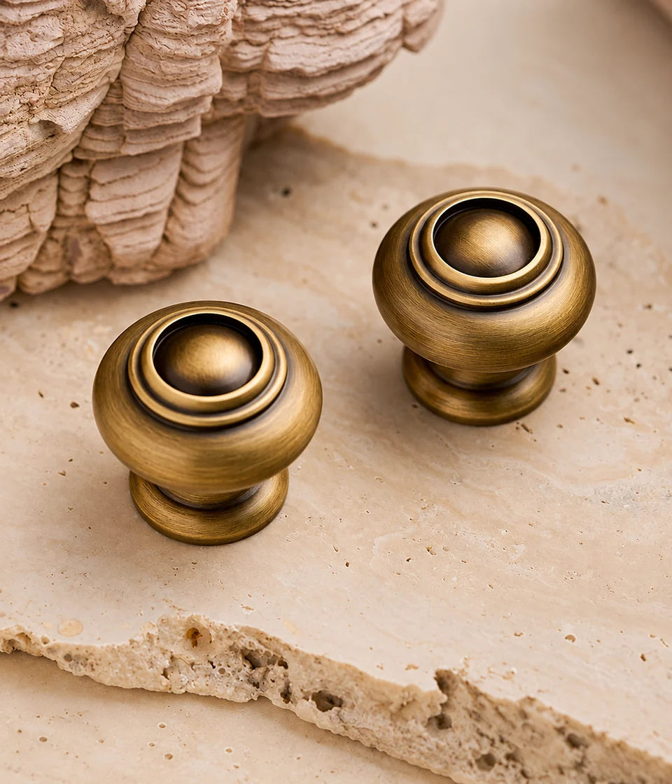 Antique brass ringed dome cabinet knobs arranged on pale stone