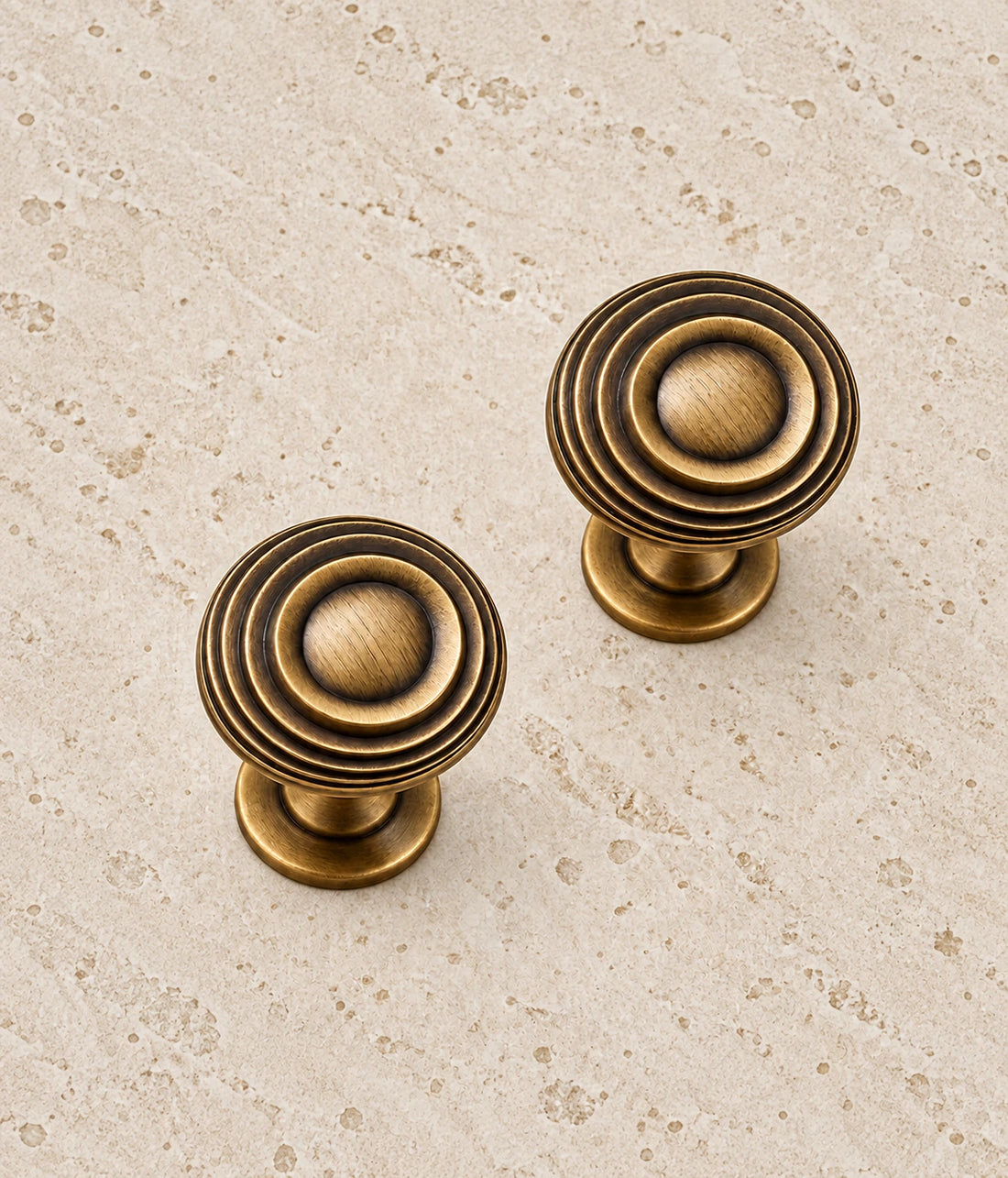 Antique Brass Ringed Pedestal Cabinet Knob on warm limestone