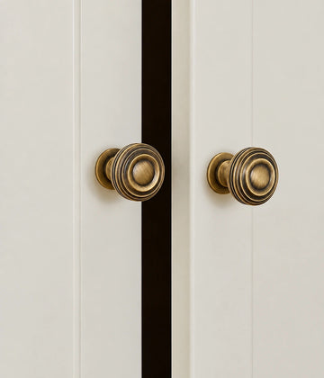 Antique brass ringed pedestal knobs mounted on white cabinet doors