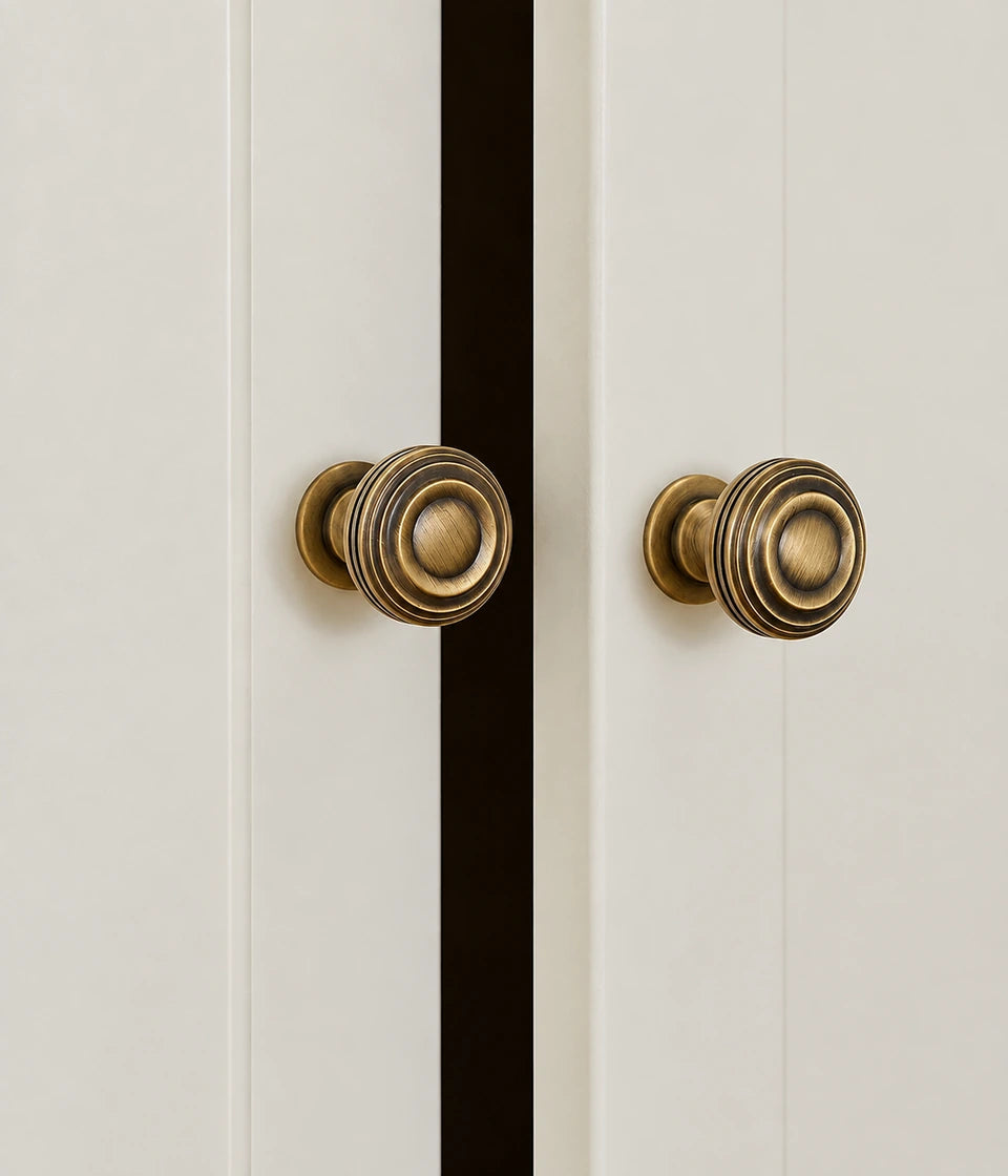 Antique brass ringed pedestal knobs mounted on white cabinet doors