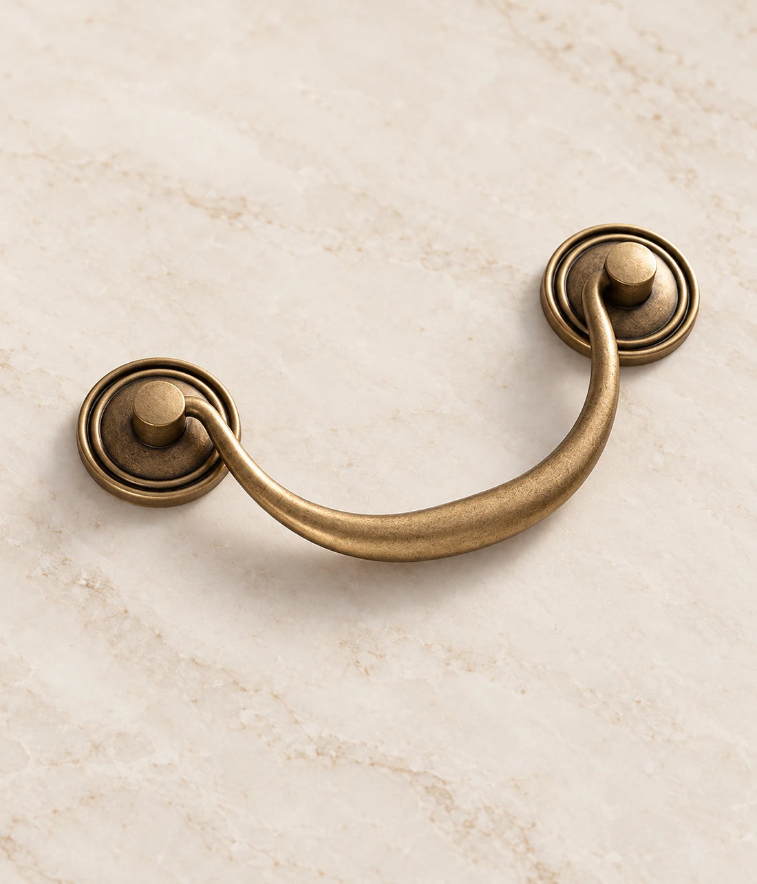 Antique brass bail pull with round ringed backplates on ivory limestone