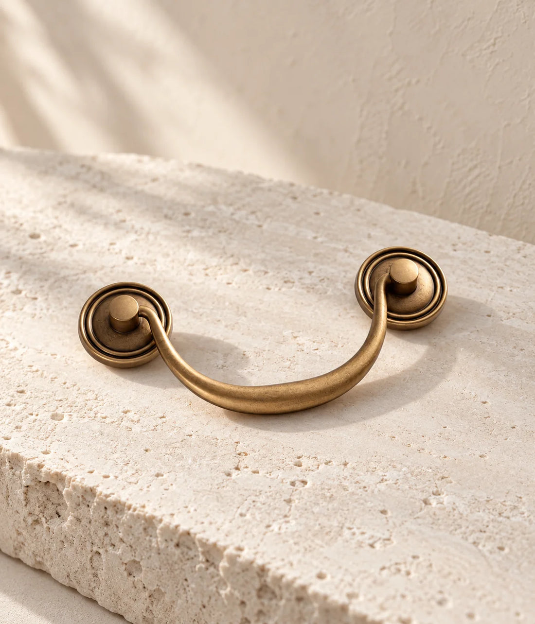 Antique brass bail pull with round ringed backplates on ivory limestone