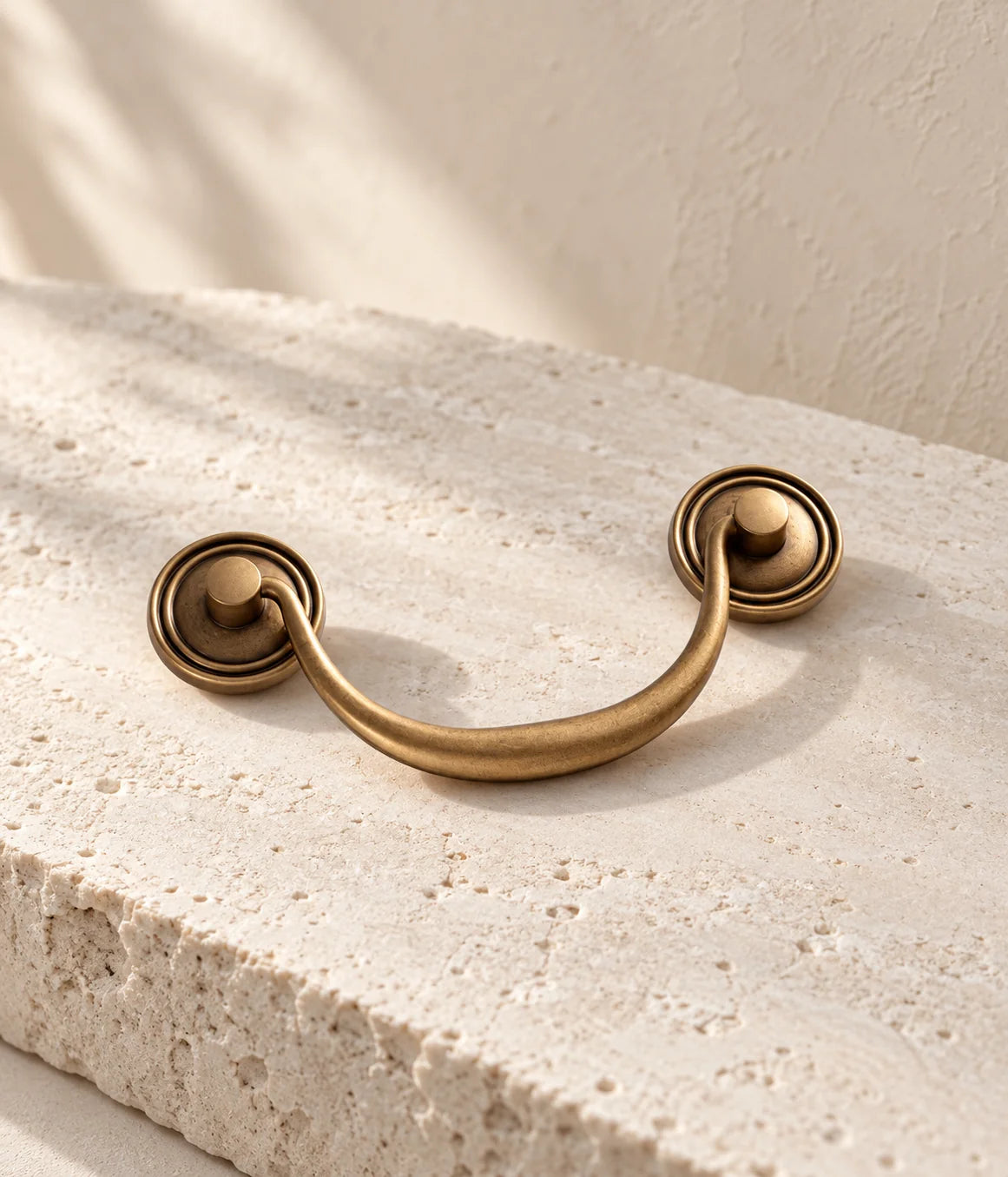 Antique brass bail pull with round ringed backplates on ivory limestone
