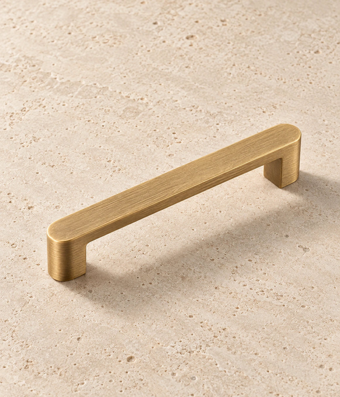 Antique Brass Rounded Cabinet Pulls arranged on warm limestone