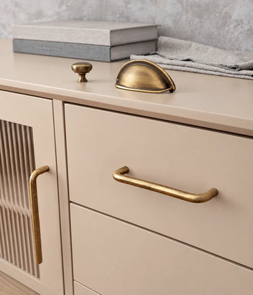 Antique brass rounded cabinet pull on a cream drawer with matching cup pull and knob