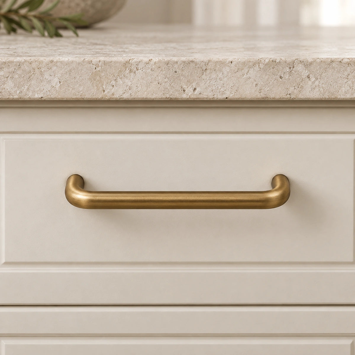 Antique brass rounded cabinet pull mounted on an ivory drawer