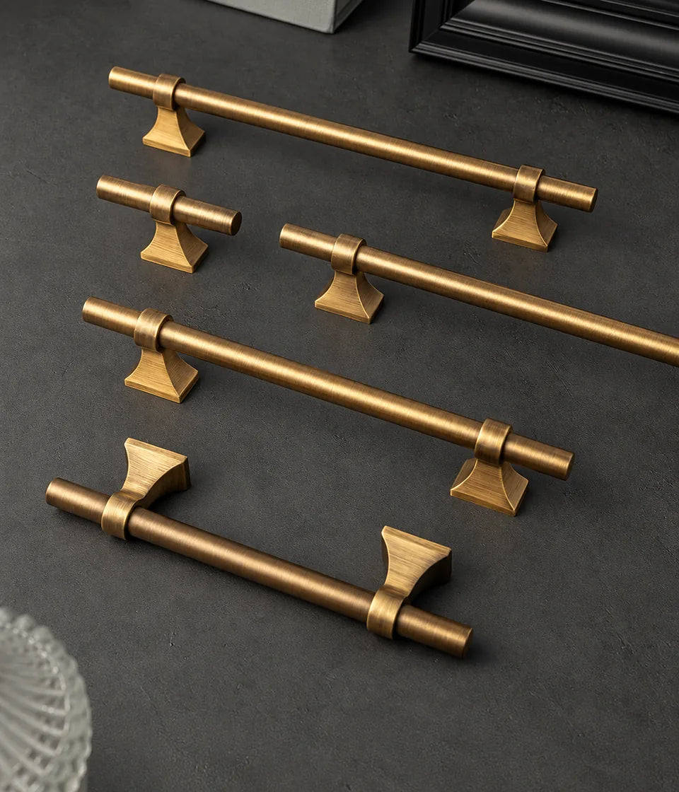 Antique brushed brass saddle-base cabinet pulls and matching T-knob arranged on a dark surface