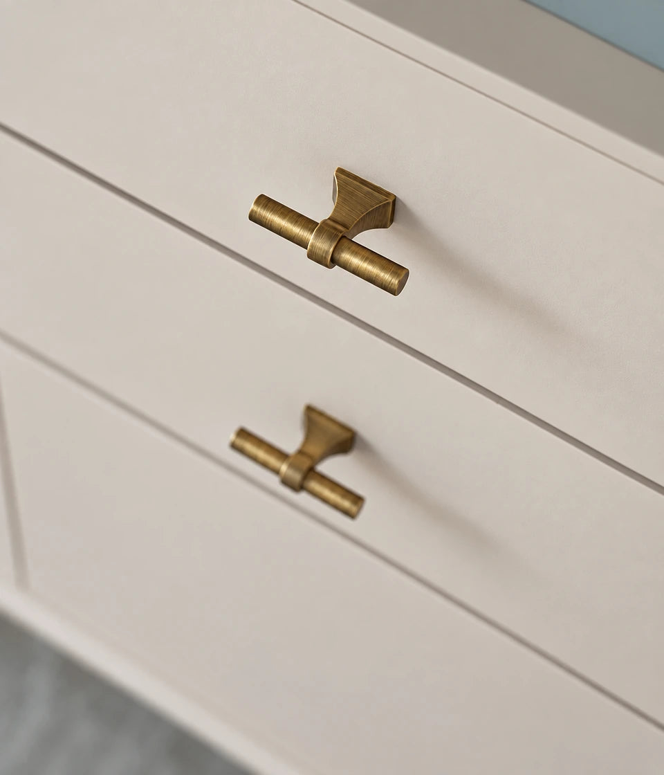 Antique brass saddle-base T-knobs installed on cream cabinet drawers