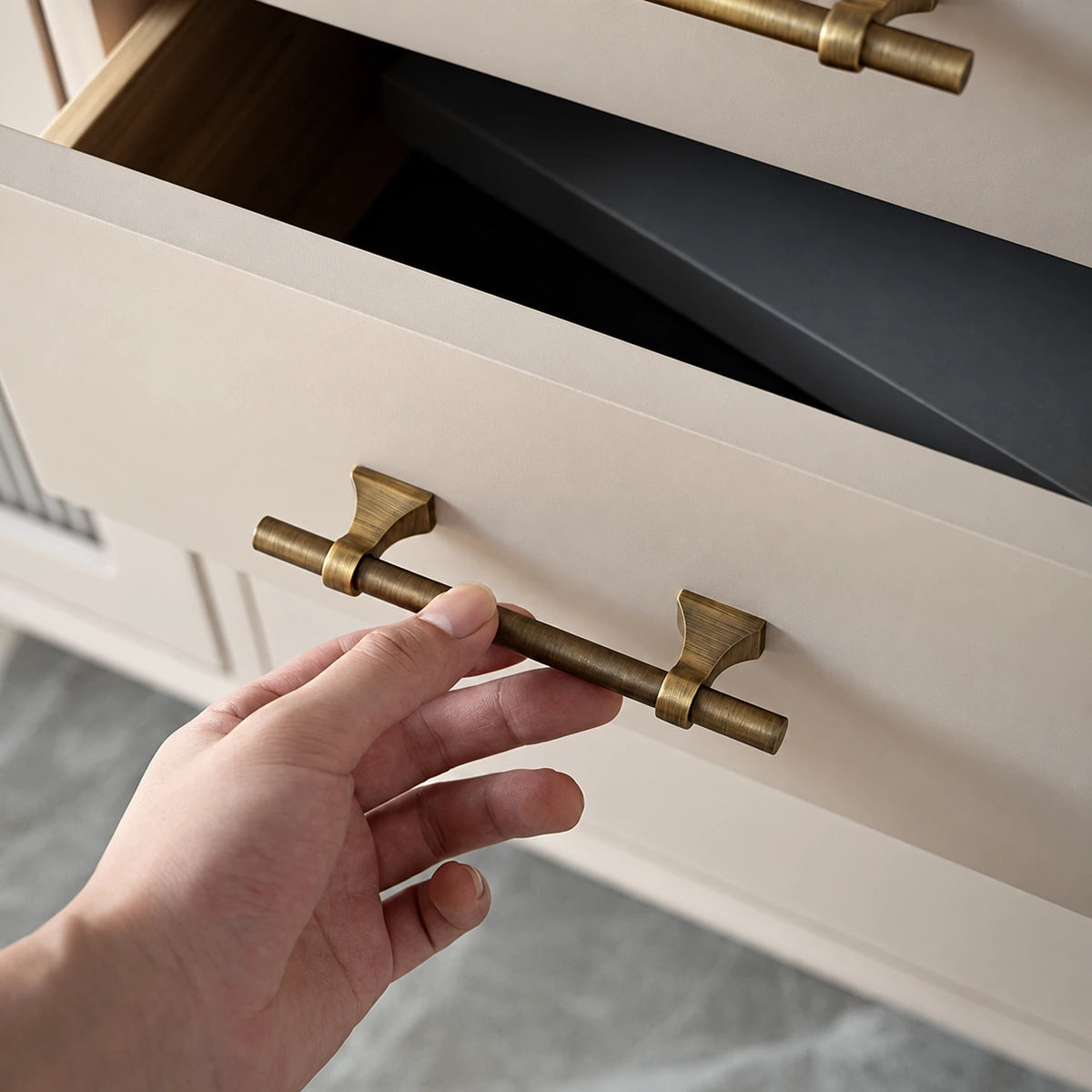 Hand opening a drawer with an antique brass saddle-base cabinet pull