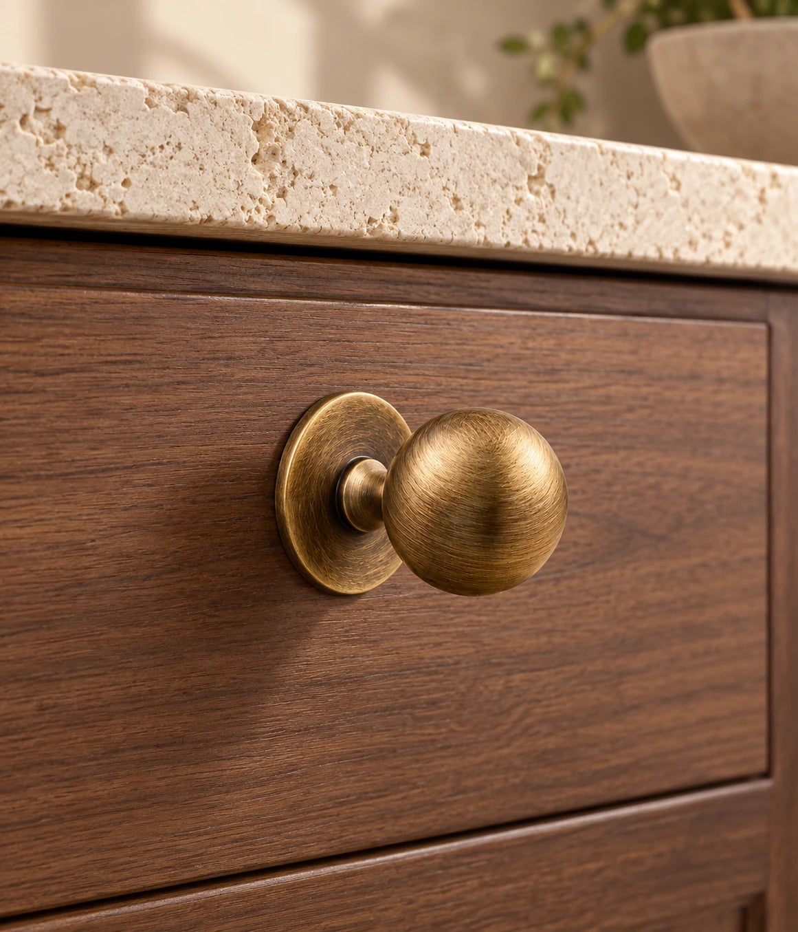 Antique Brass Saucer-Base Ball Cabinet Knob installed on a walnut cabinet drawer