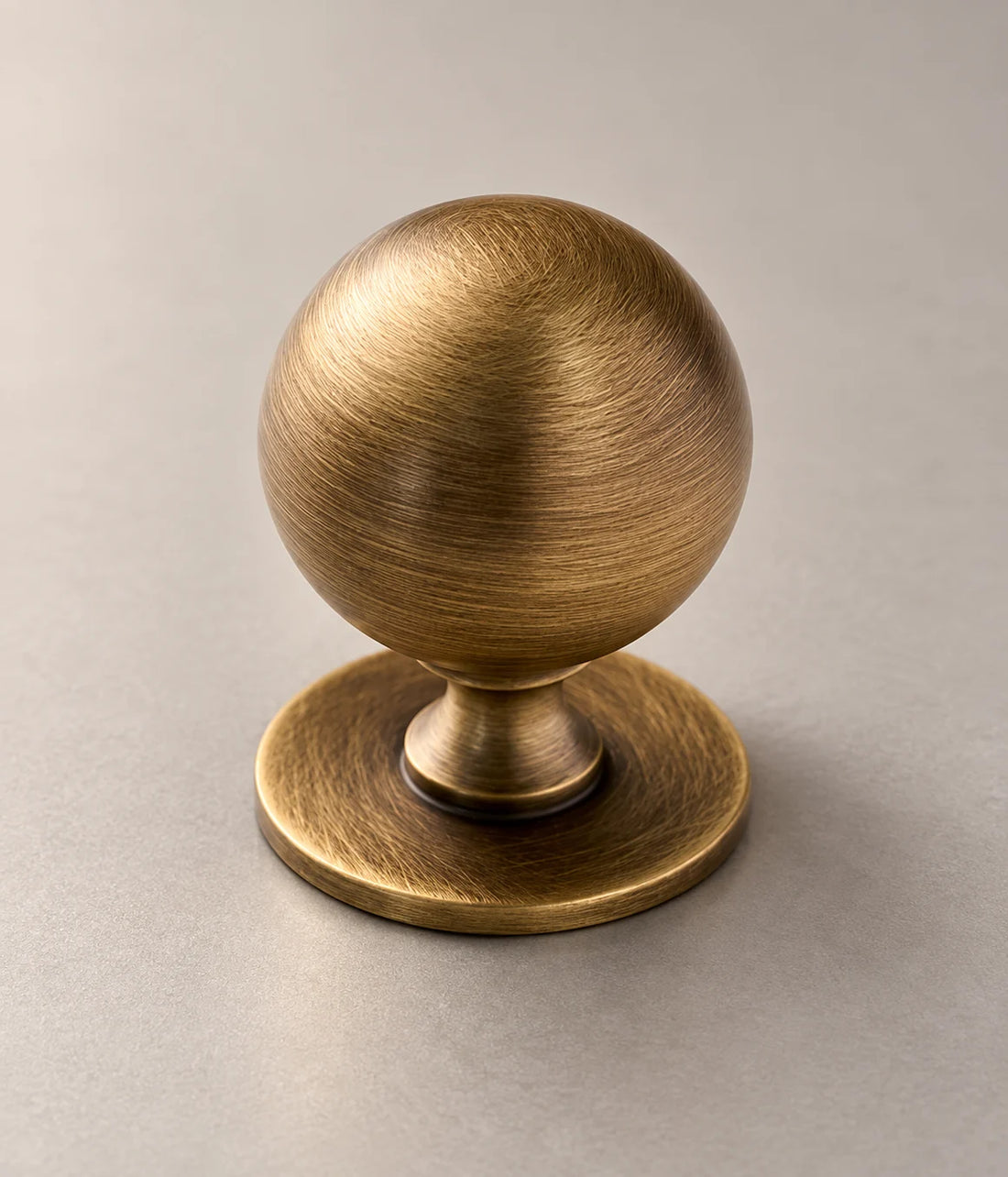 Antique brass ball cabinet knobs with broad round bases on warm limestone