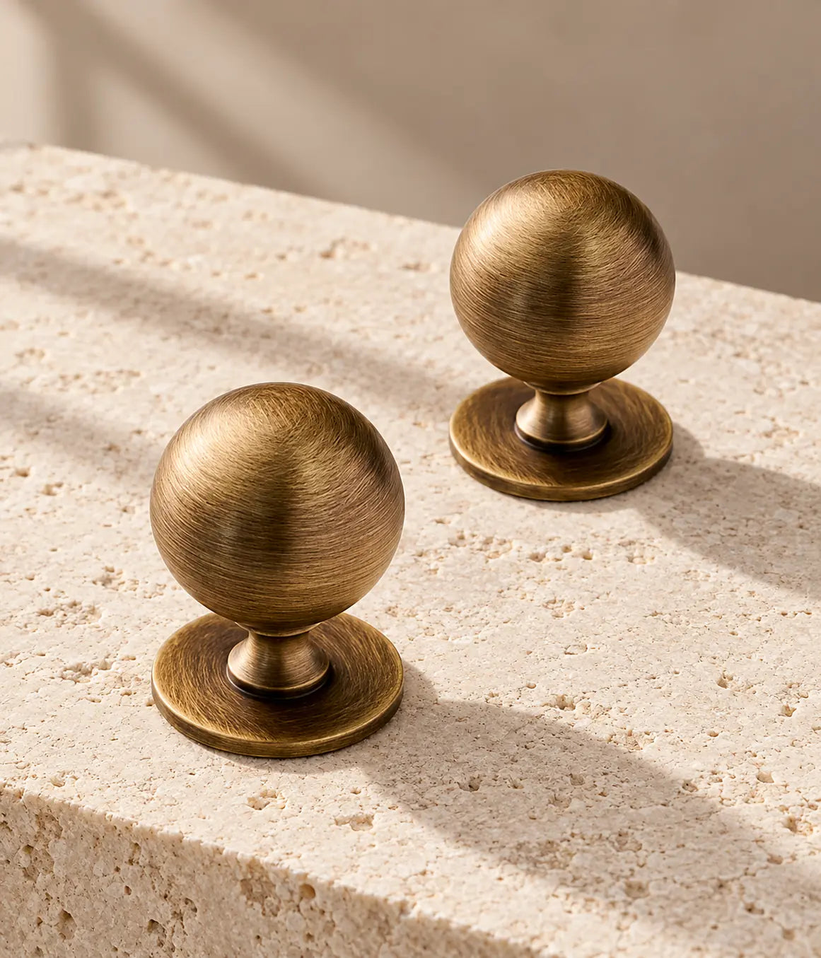 Antique brass ball cabinet knobs with broad round bases on warm limestone