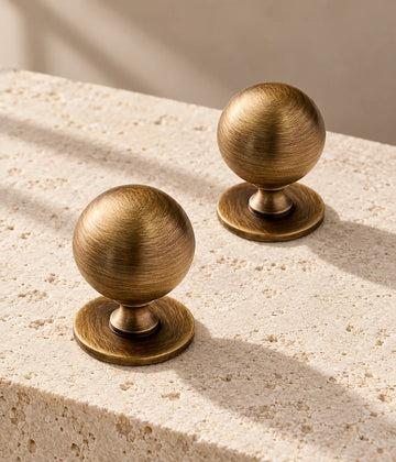 Antique brass ball cabinet knobs with broad round bases on warm limestone