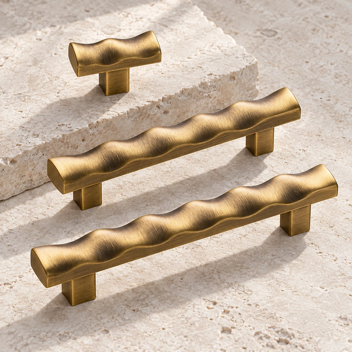 Antique brass scalloped cabinet pulls and matching T-knob arranged on limestone