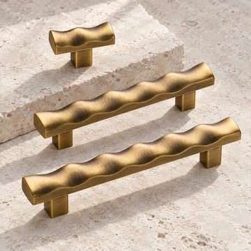 Antique brass scalloped cabinet pulls and matching T-knob arranged on limestone