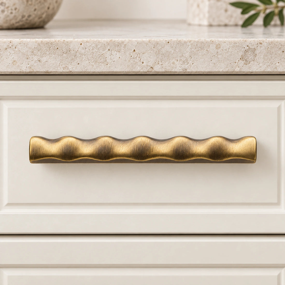 Antique brass scalloped cabinet pulls and matching T-knob arranged on limestone