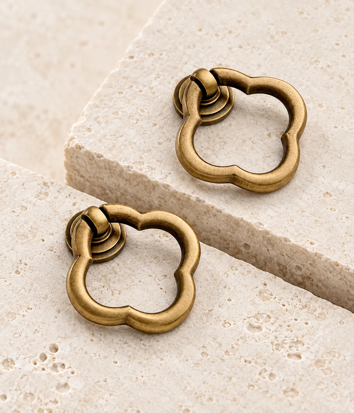 Antique brass scalloped ring pulls arranged on warm limestone