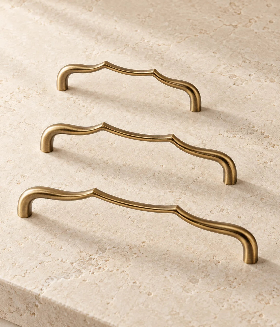 Three antique brass sculpted arch cabinet pulls arranged on warm limestone