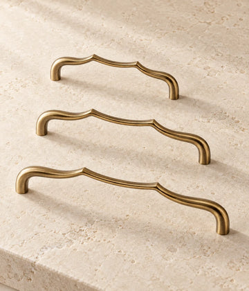 Three antique brass sculpted arch cabinet pulls arranged on warm limestone