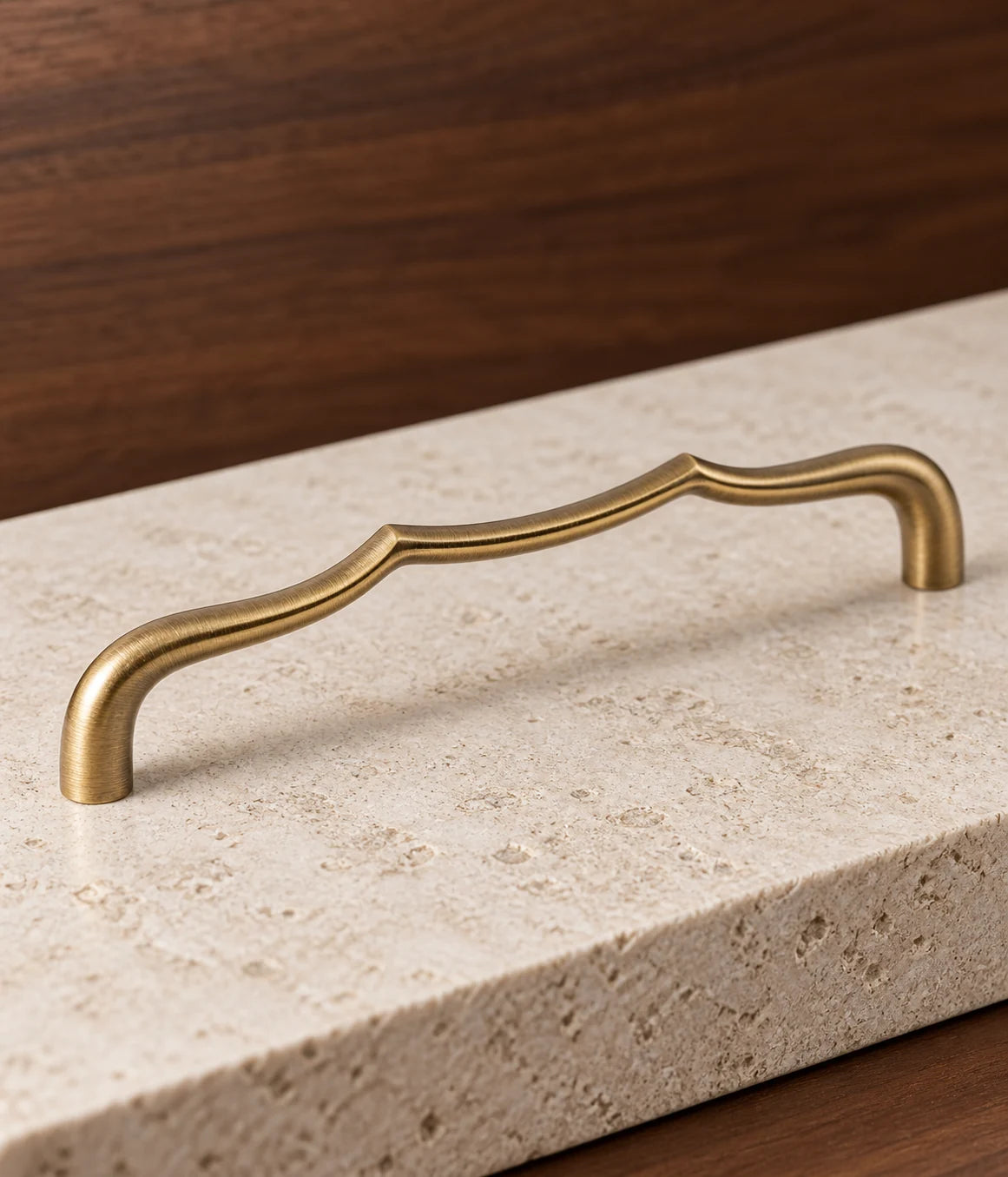 Curved grip and raised shoulders of an antique brass sculpted arch cabinet pull