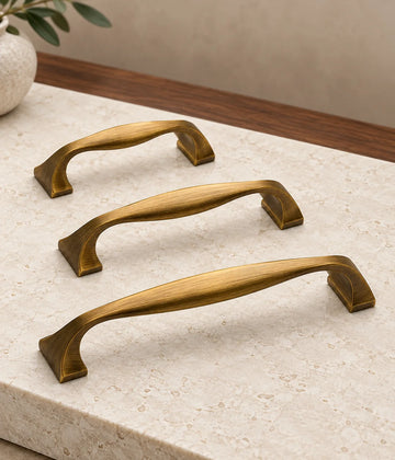 Three antique brass sculpted bow cabinet pulls arranged on pale limestone with a walnut background