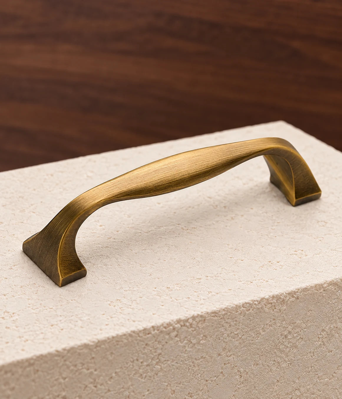 Close view of an antique brass sculpted bow cabinet pull showing its brushed grip and flared feet