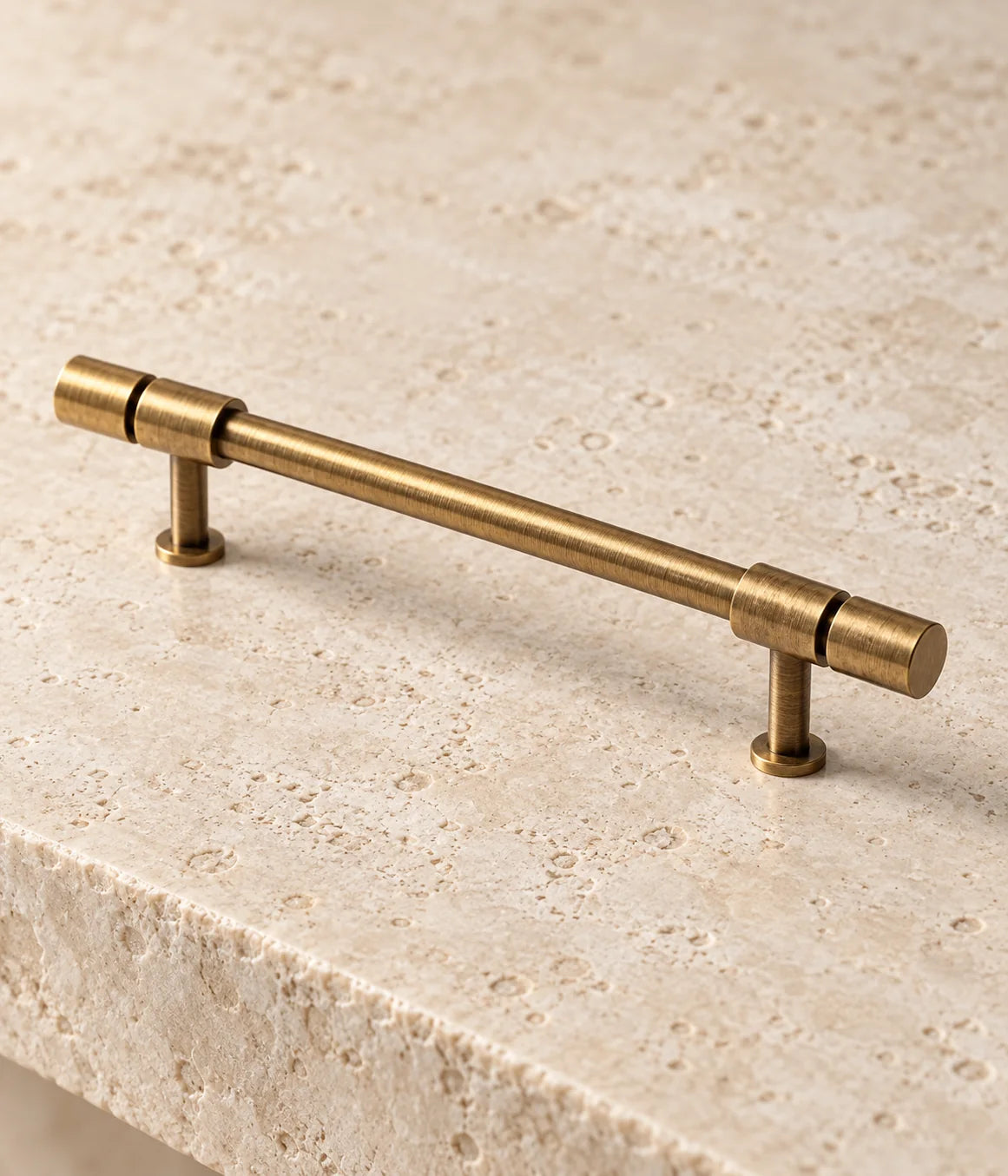 Antique brass pull with thick cylindrical end caps separated by recessed seams from its mounting collars