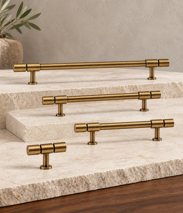 Antique brass segmented-end cabinet pulls and T-knob arranged on pale limestone and walnut