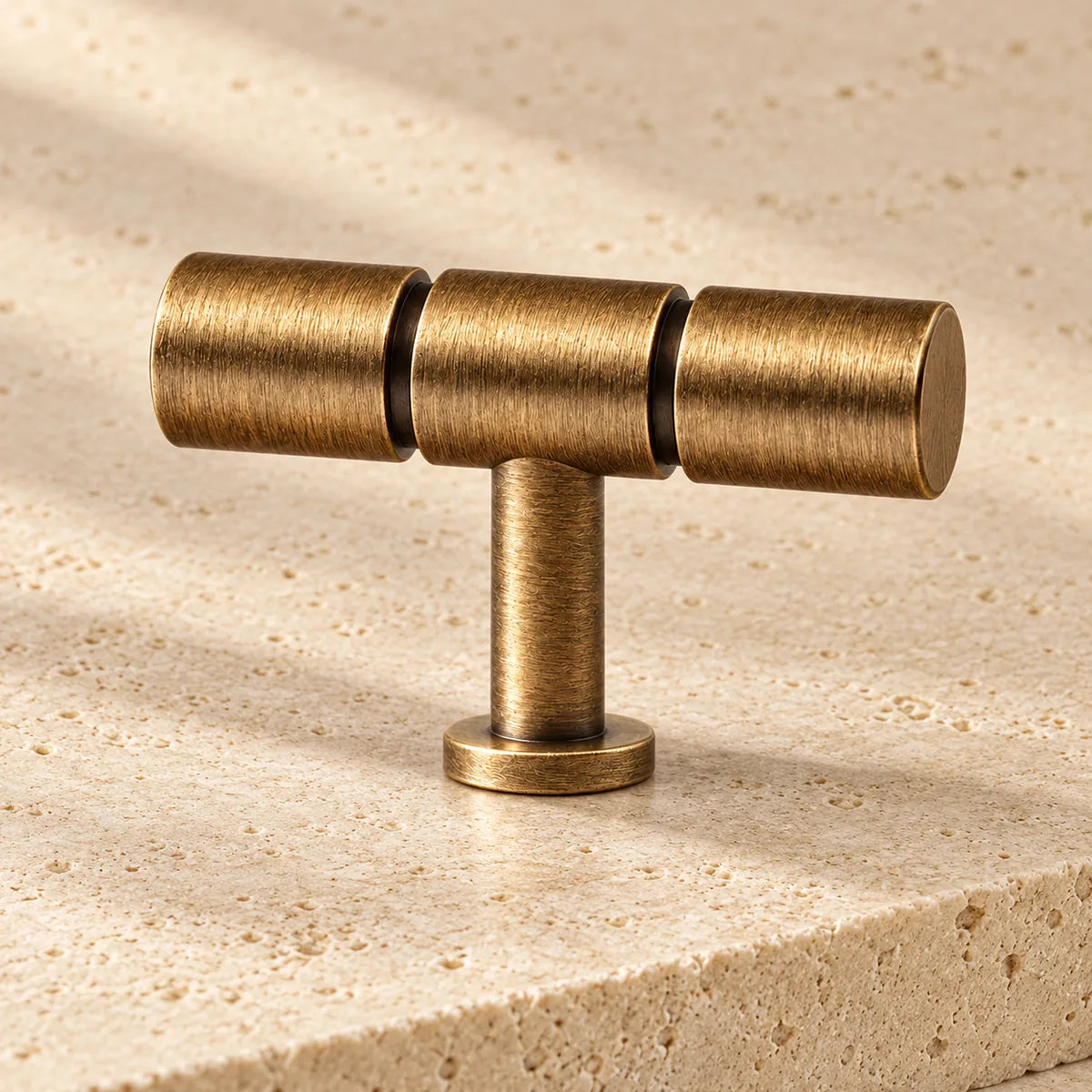 antique brass segmented t bar cabinet knob on pale limestone.